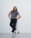 Woman standing against a white wall wearing a patterned shirt and black pants.