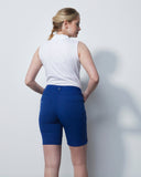 Woman wearing a white sleeveless top and blue shorts against a plain background