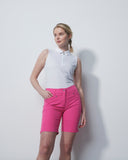 Woman wearing a white sleeveless top and pink shorts against a plain background