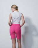 Woman wearing a white sleeveless top and pink shorts against a plain background