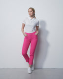 Woman wearing a white polo shirt and pink pants against a plain background