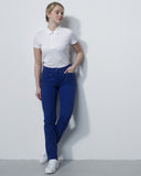 Woman wearing a white polo shirt and blue pants against a plain background