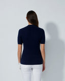 Person wearing a navy blue sweater and white pants against a light gray background