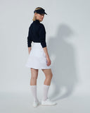 Person wearing a black top, white skirt, and white socks on a plain background