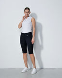 Woman wearing a white sleeveless top and navt shorts against a plain background